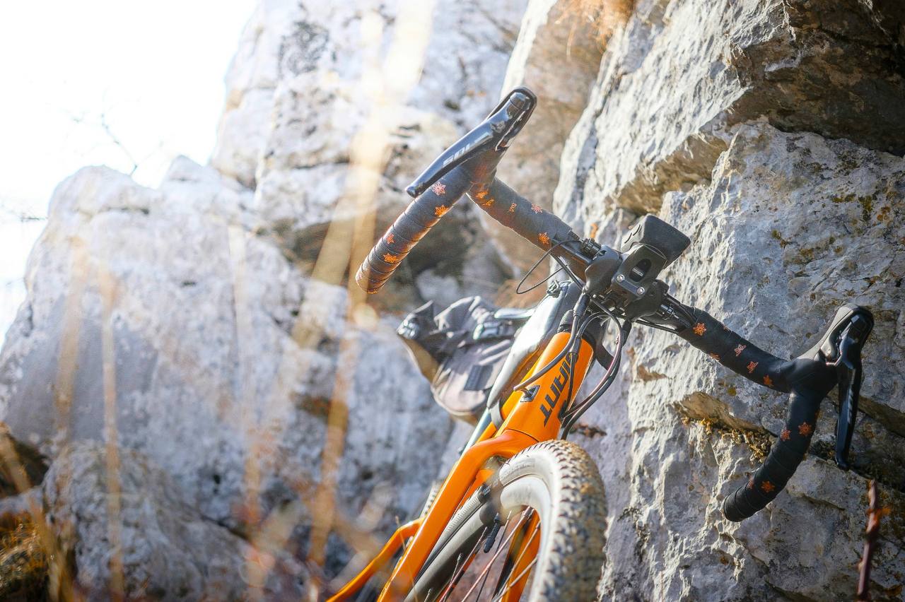 Gros plan sur le cintre d'un vélo gravel orange, appuyé contre une paroi rocheuse